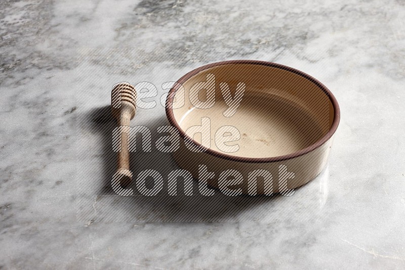 Beige Pottery Oven Bowl with wooden honey handle on the side with grey marble flooring, 45 degree angle