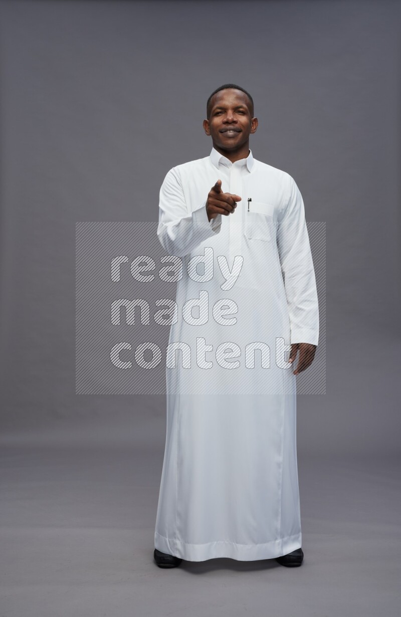 Saudi man wearing thob standing interacting with the camera on gray background