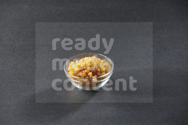 A glass bowl full of raisins on a black background in different angles