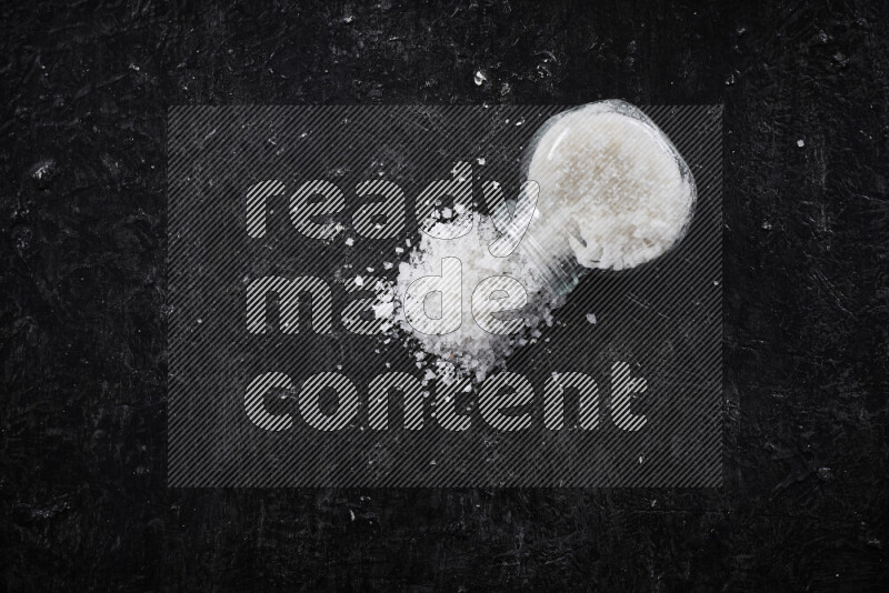 A glass jar full of coarse sea salt crystals on black background