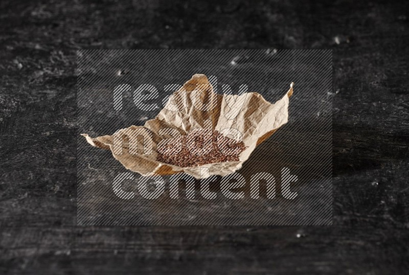 A crumpled piece of paper full of flax on a textured black flooring in different angles