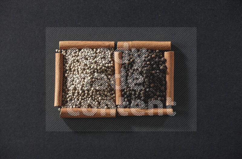 مربعان من أعواد القرفة ممتلئان بحبوب الفلفل الأبيض وحبوب الفلفل الأسود علي خلفية سوداء