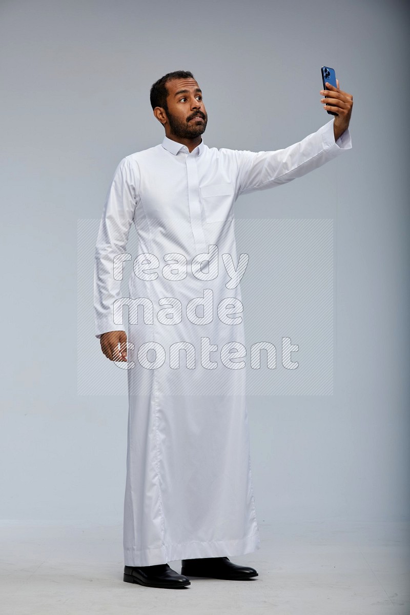 Saudi man wearing Thob standing taking selfie on Gray background