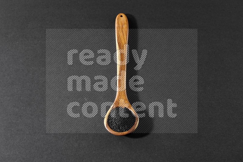 A wooden ladle full of black seeds on a black flooring