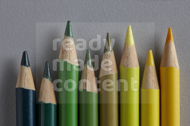 A collection of sharpened colored pencils arranged showcasing a gradient of yellow and green hues on grey background