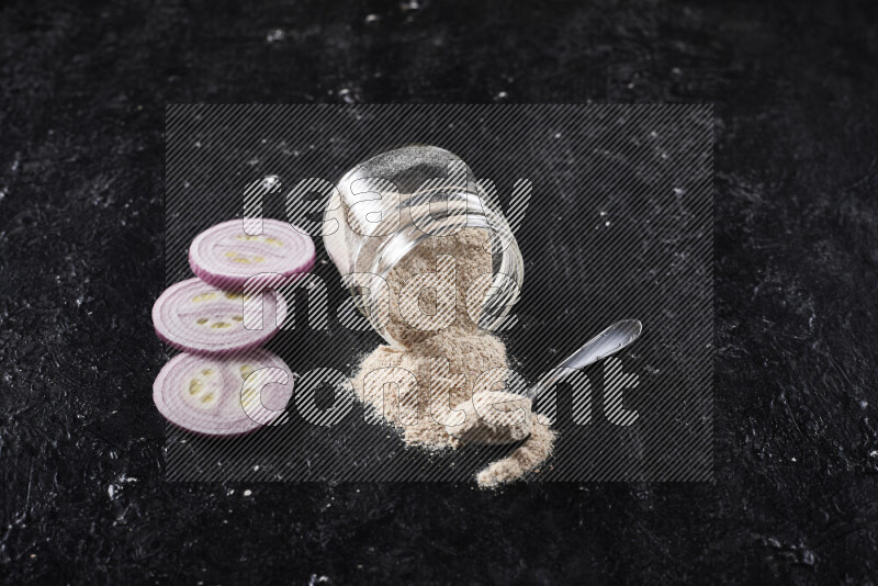 A glass jar full of onion powder flipped with some spilling powder on black background