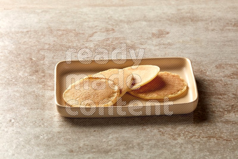 Four stacked plain mini pancakes in a rectangular plate on beige background