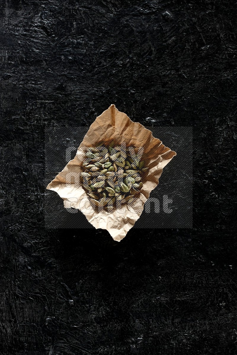 Cardamom seeds in a crumpled piece of paper on textured black flooring