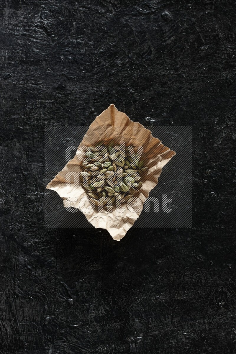 Cardamom seeds in a crumpled piece of paper on textured black flooring