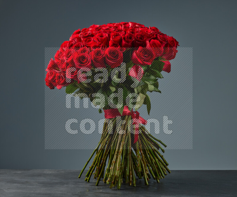 باقة فاخرة من الورود الحمراء المربوطة بإحكام بشريط أحمر على خلفية من الرخام الأسود