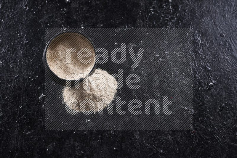 وعاء فخاري اسود ممتلئ ببودرة البصل مقلوب مع بعض البودرة المتناثره منه على خلفية سوداء