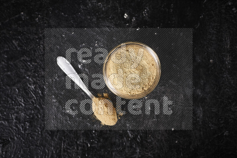 A glass jar full of ground ginger powder on black background