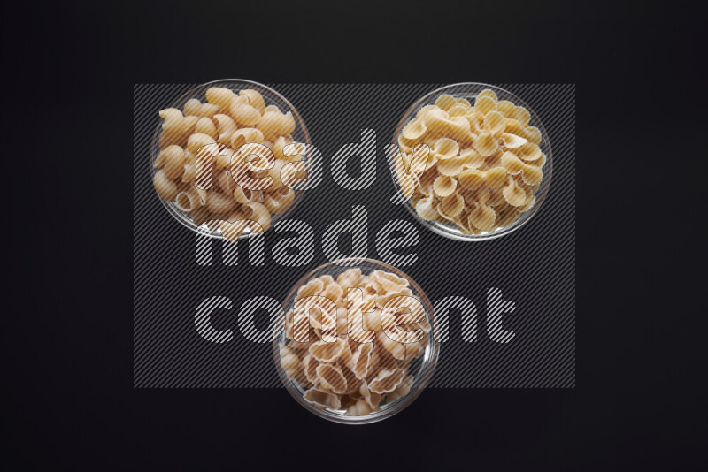 Different pasta types in glass bowls on black background