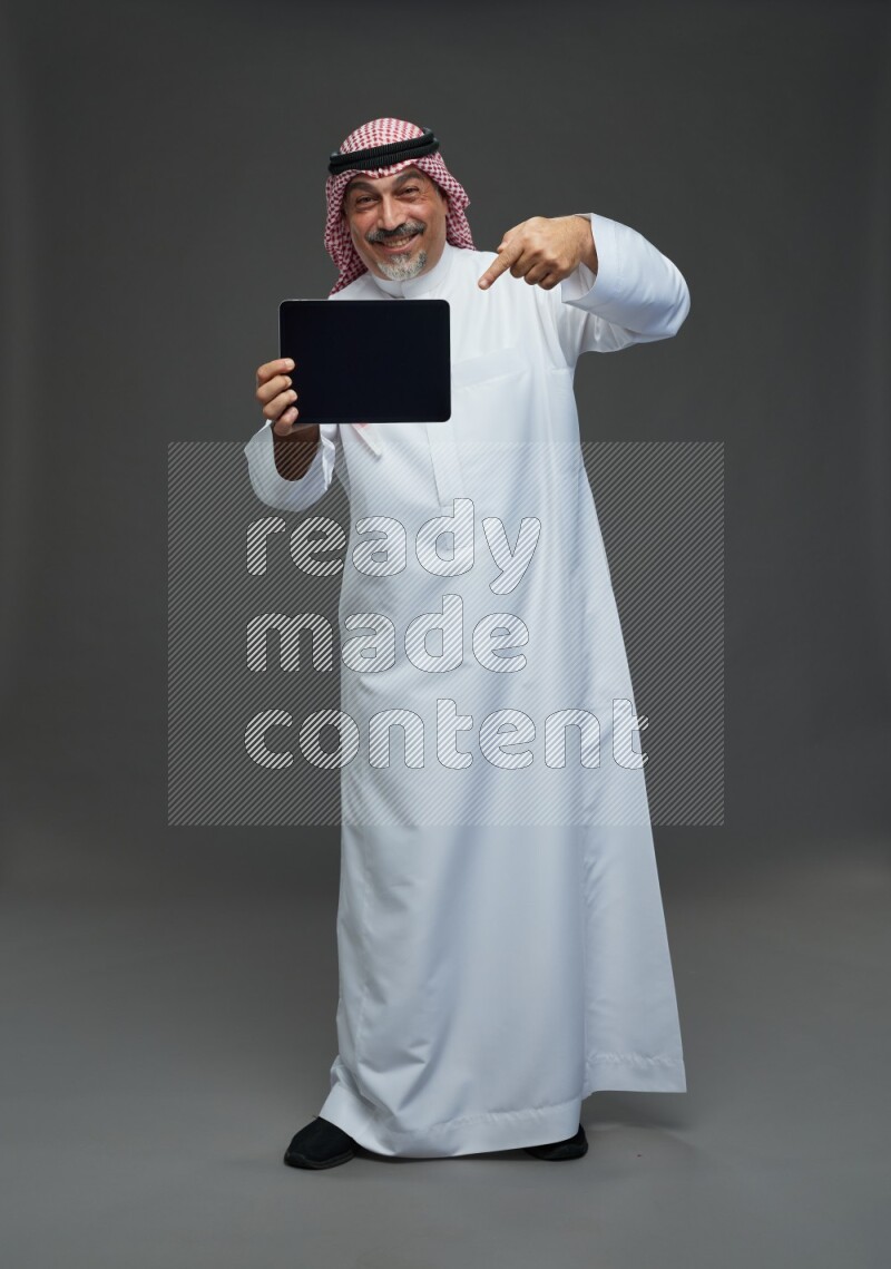 Saudi man with shomag Standing working on tablet on gray background