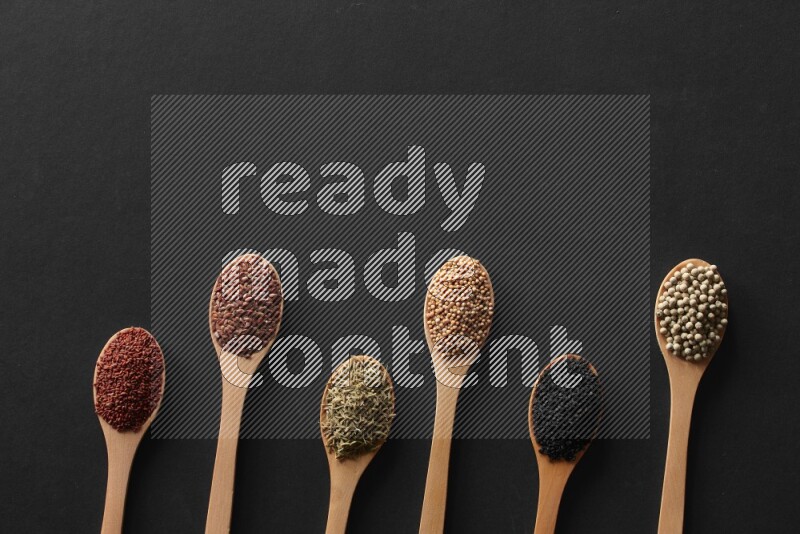 الفلفل الأسود وحبوب الخردل وحبة البركة وحب الرشاد والكمون و حبوب الكتان في معالق خشبية علي خلفية سوداء