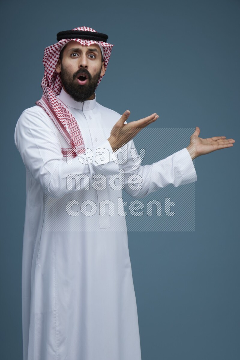 A man pointing in a blue background wearing Saudi Thob and Shomag