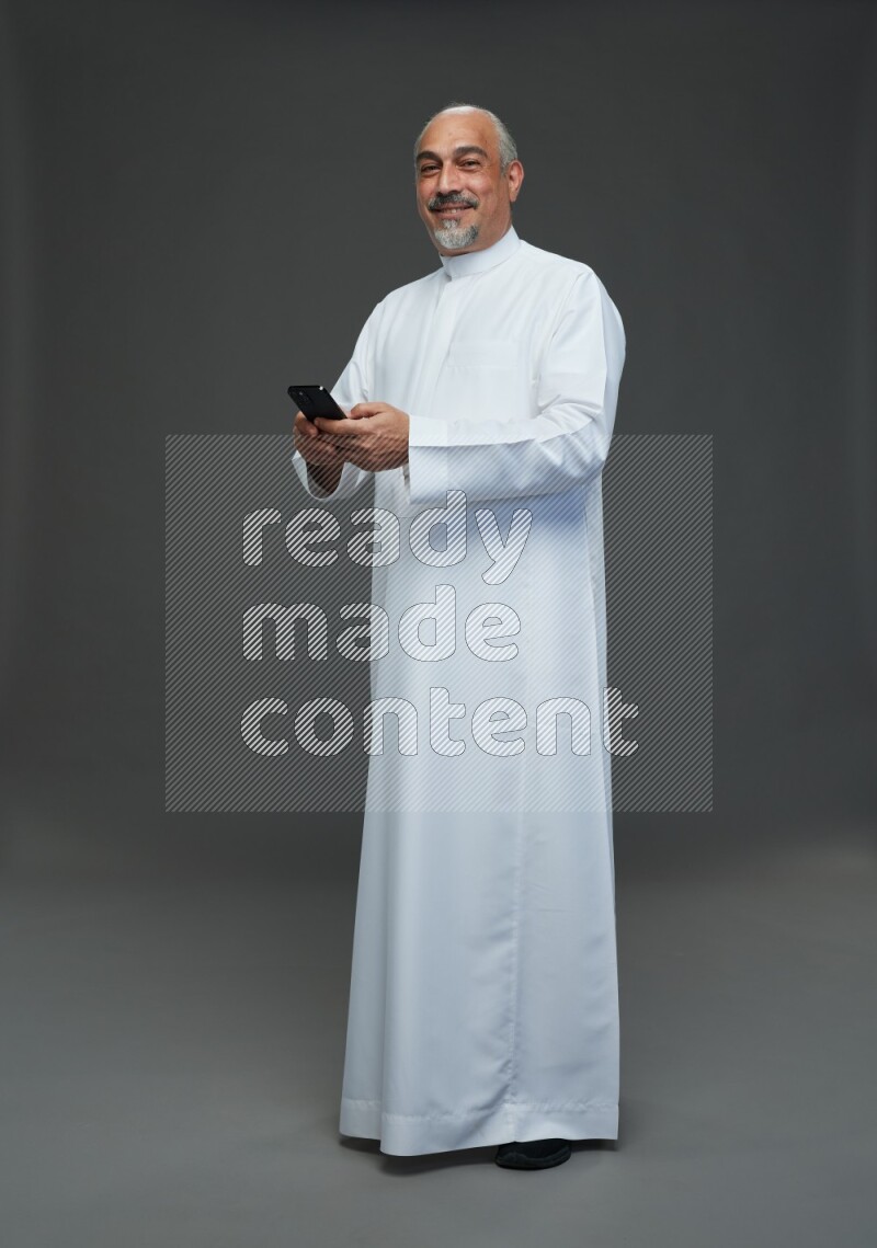 Saudi man without shomag Standing texting on phone on gray background