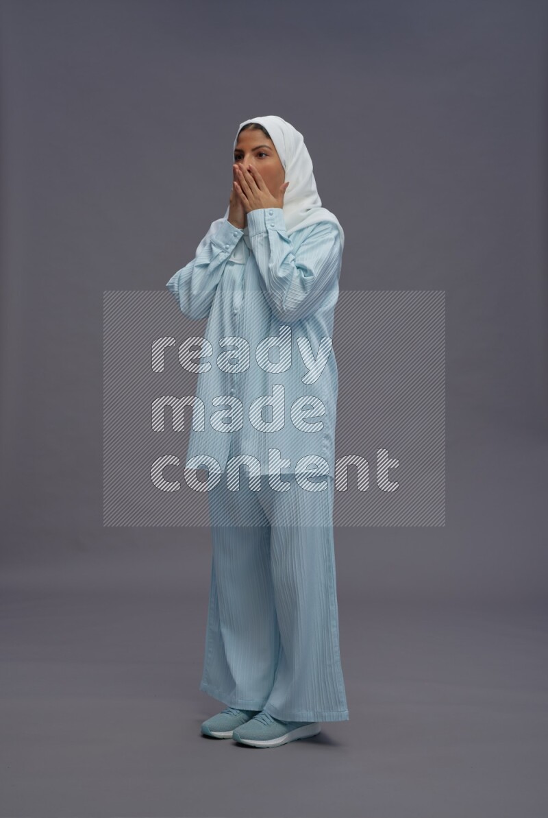 Saudi woman wearing hijab clothes standing interacting with the camera on gray background