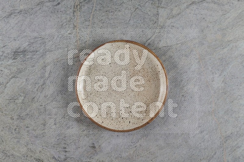 Top View Shot Of A Beige Pottery Circular Plate On Grey Marble Flooring