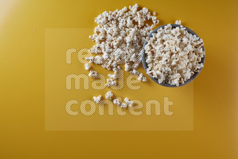 A multicolored pottery bowl full of popcorn with popcorn beside it on a yellow background in different angles
