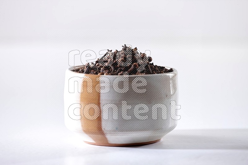 A beige ceramic bowl full of cloves on a white flooring