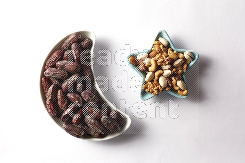 Dates in a crescent pottery plate and a star shaped plate with mixed nuts on white background