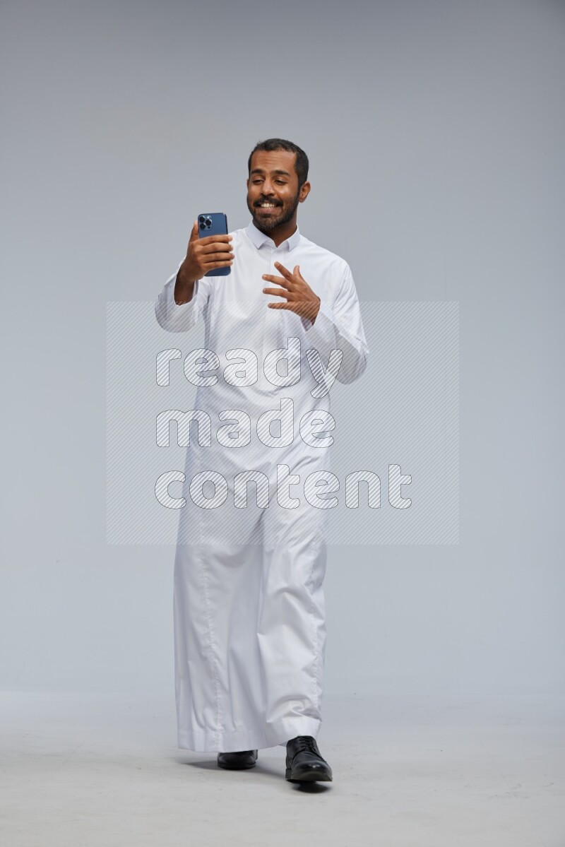 Saudi man wearing Thob standing taking selfie on Gray background