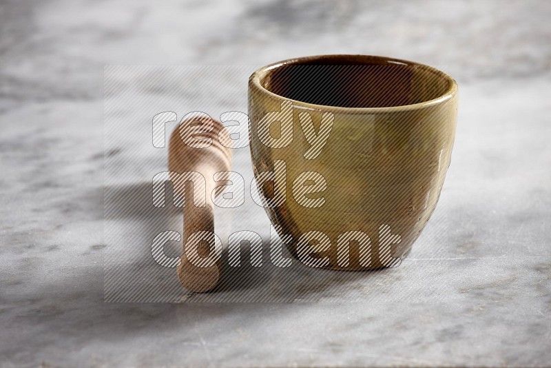 Multicolored Pottery cup with wooden honey handle on the side with grey marble flooring, 15 degree angle