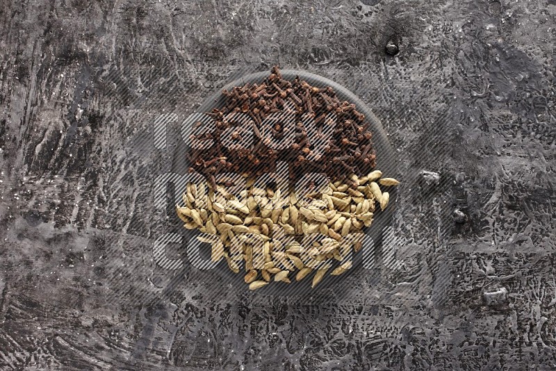 Cardamom and cloves on a black plate on textured black background