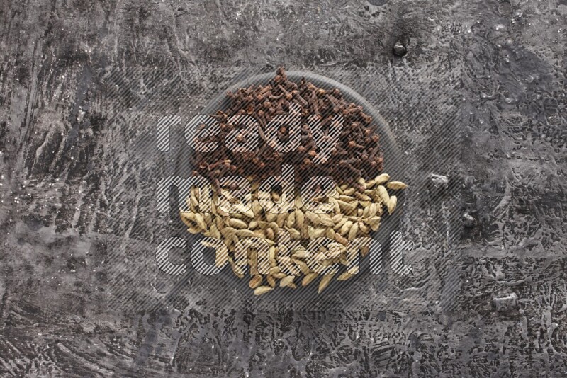 Cardamom and cloves on a black plate on textured black background