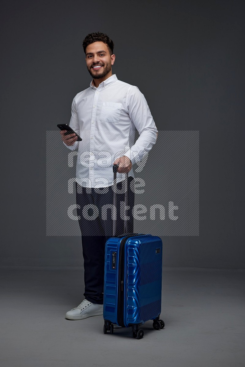 A man wearing smart casual holding luggage eye level on a gray background