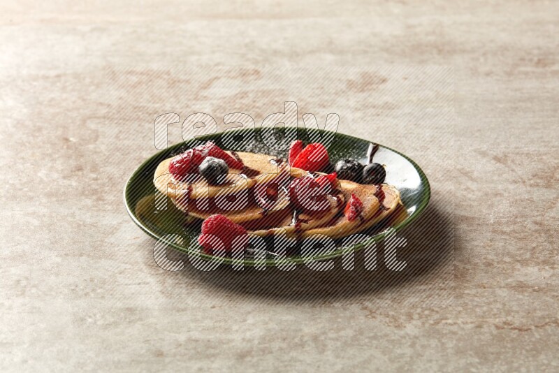 Five stacked mixed berries mini pancakes in a green plate on beige background