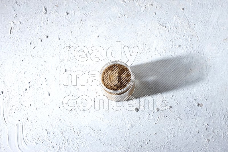 A glass jar full of allspice powder on a textured white flooring