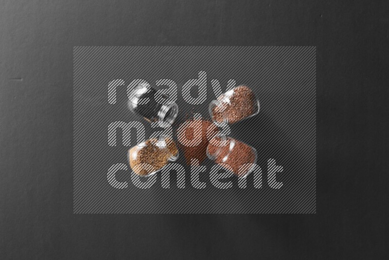 4 glass spice jars full of black seeds, mustard seeds, flax and garden cress on black flooring