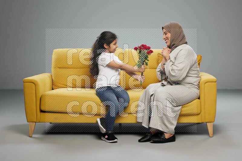 A girl sitting giving flowers to her mother on gray background