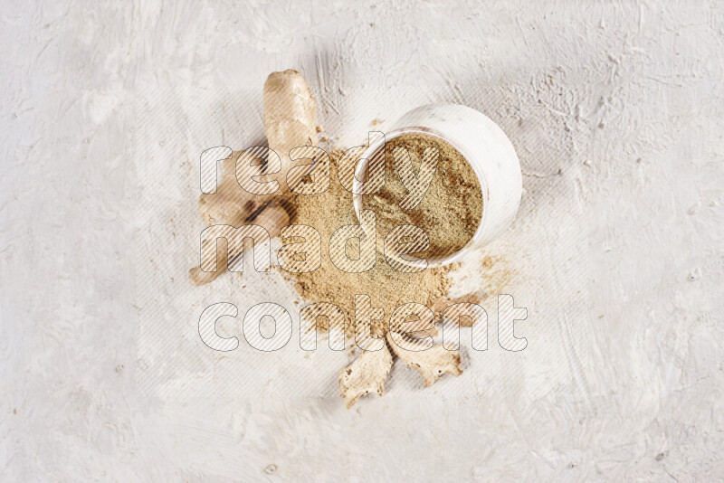 A beige pottery bowl full of ground ginger powder with fallen powder from it on white background