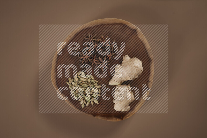 An assorted whole spices on a flat wooden tray including fresh and dried ginger, cinnamon sticks, cardamom, turmeric fingers, cloves, star anise on beige background