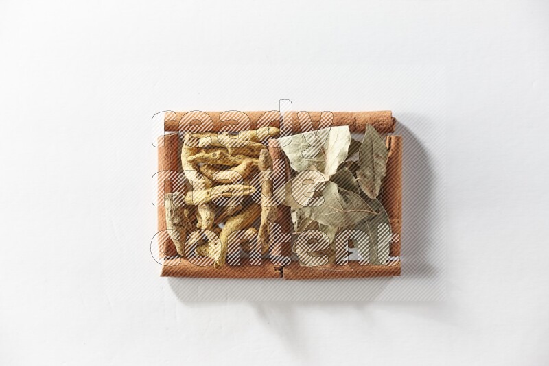 مربعان من أعواد القرفة ممتلئان بأصابع الكركم وأوراق الغار علي خلفية بيضاء