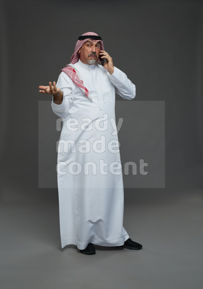 Saudi man with shomag Standing talking on phone on gray background