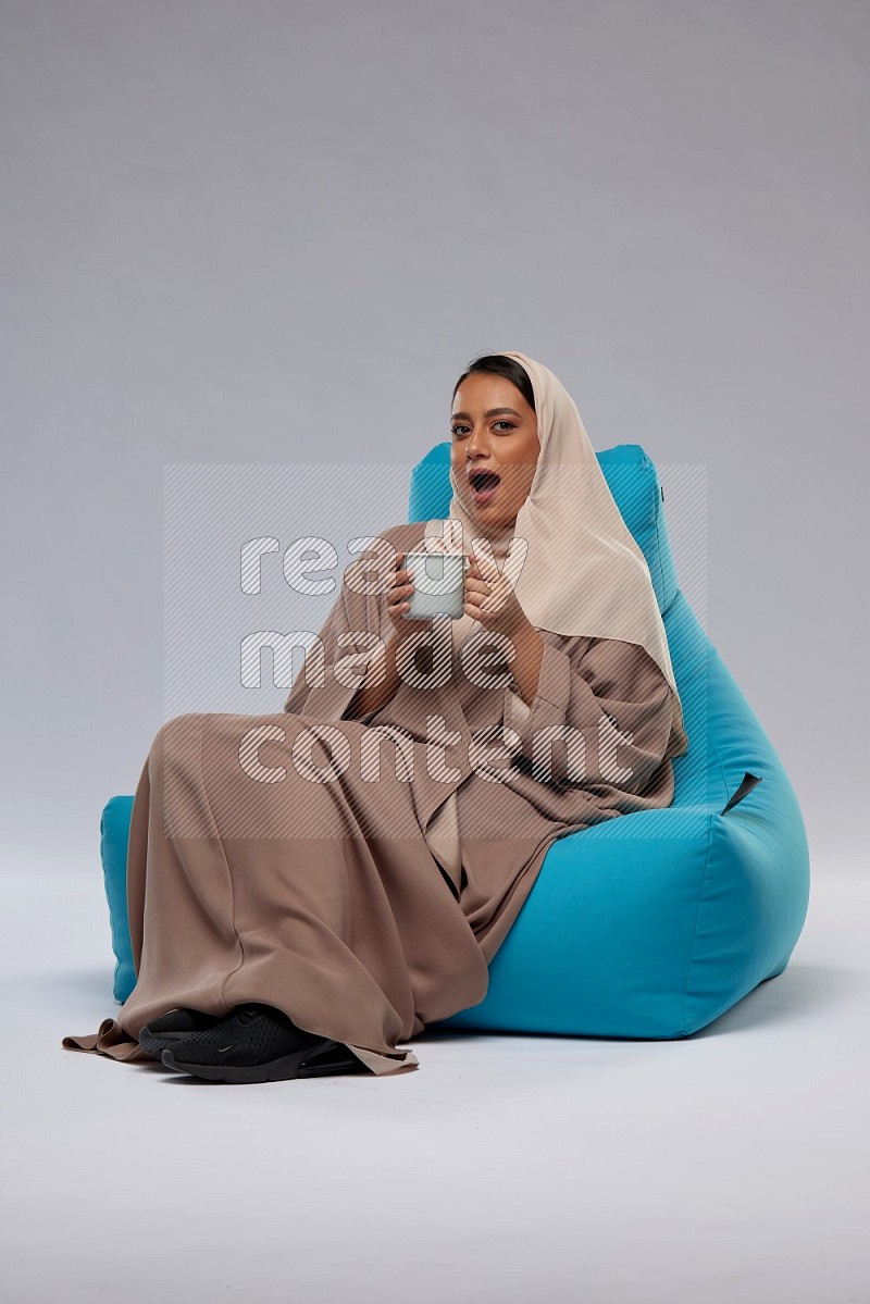 A Saudi woman sitting on a blue beanbag and drinking coffee