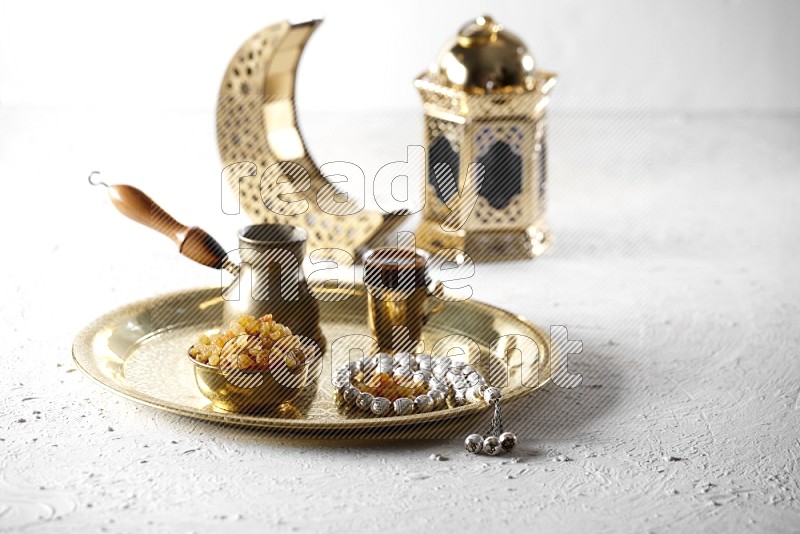 Raisins in a metal bowl with coffee and prayer beads on a tray beside lanterns in a light setup