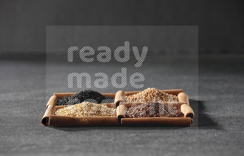 4 squares of cinnamon sticks full of black seeds, sesame, flaxseeds and mustard seeds on black flooring