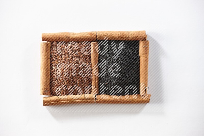 مربعان من أعواد القرفة ممتلئان ببذور الكتان وحبة البركة السوداء علي خلفية بيضاء