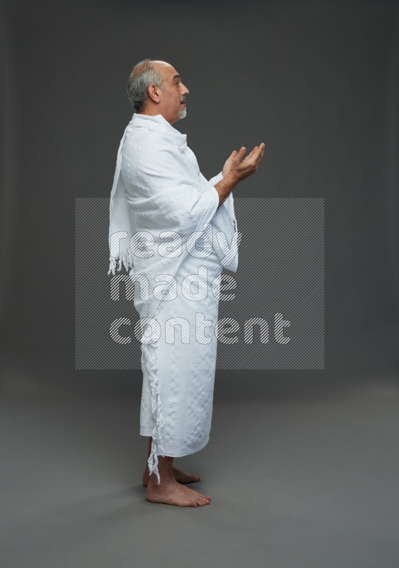 A man wearing Ehram Standing dua'a on gray background