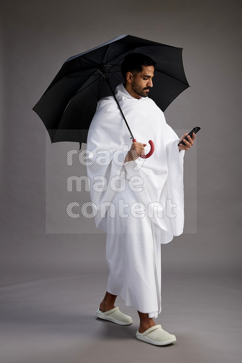 A man wearing Ehram Standing holding umbrella on gray background