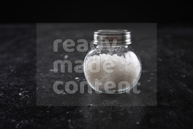 A glass jar full of coarse sea salt crystals on black background