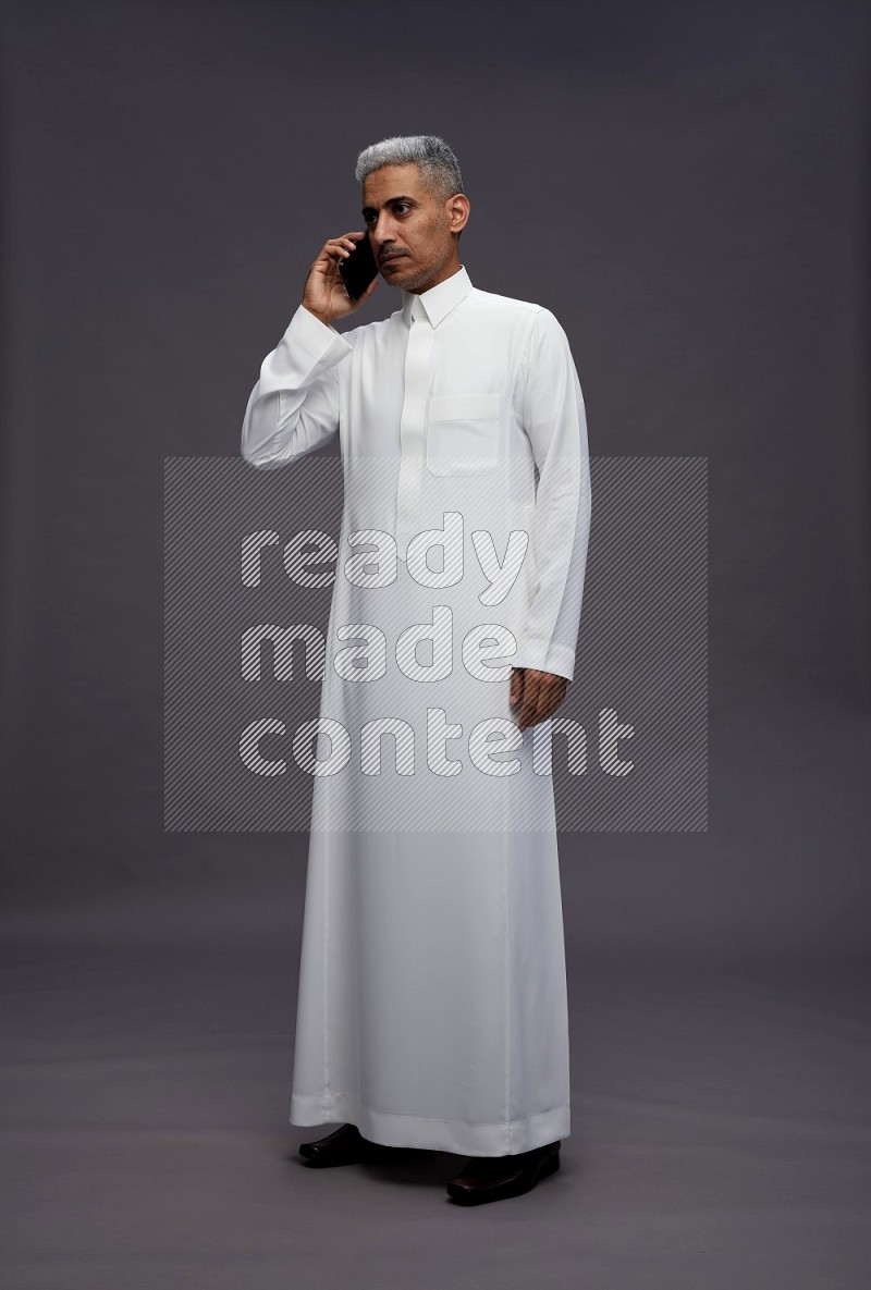 Saudi man wearing thob standing talking on phone on gray background