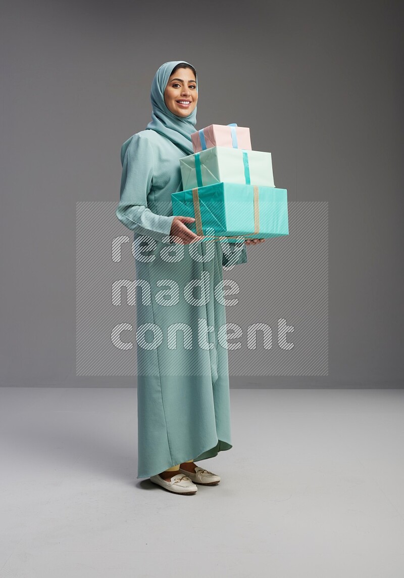 Saudi Woman wearing Abaya standing holding gift box on Gray background