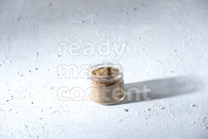 A glass jar full of allspice powder on a textured white flooring