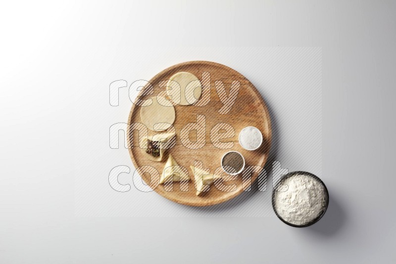 two closed sambosas and one open sambosa filled with meat while flour, salt, and black pepper aside in a wooden dish on a white background